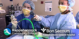 Group of students and an instructor wearing blue disposable gowns stand in a lab classroom.